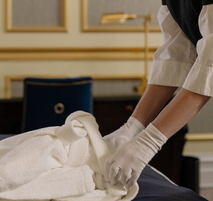 Housekeeper arranging bed linens in a luxurious hotel room, demonstrating professional care.